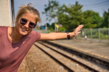 Sarışın bir kız, güneş gözlüklü vücudunu trenden çıkartıyor, bir tutamağa tutunuyor ve elini uzatıyordu Tayland 'da tren raylarında özgürlüğün işareti olarak.