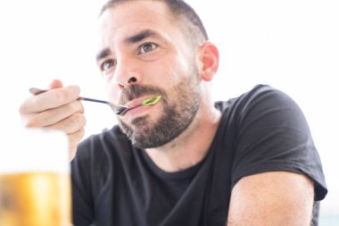 Sakallı genç adam masanın ortasında birayla salata yiyor.