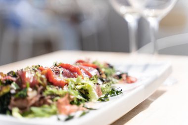 Dikdörtgen bir tabakta tütsülenmiş somon ve çekirdekli salata kristal bardaklarla dolu bir restoran masasında. Gastronomi