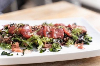 Dikdörtgen bir tabakta tütsülenmiş somon balığı ve ahşap bir restoran masasında tohumlu salata. Gastronomi