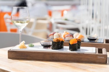 Suşi, masada bir bardak beyaz şarap ve soya sosuyla küçük tahtalarda servis edilir.