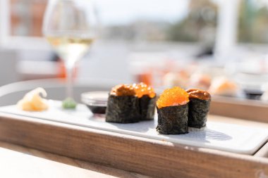 Balık yumurtalarından oluşan suşi yemeği masada bir bardak beyaz şarapla birlikte soya soslu küçük tahtalarda servis edilir.