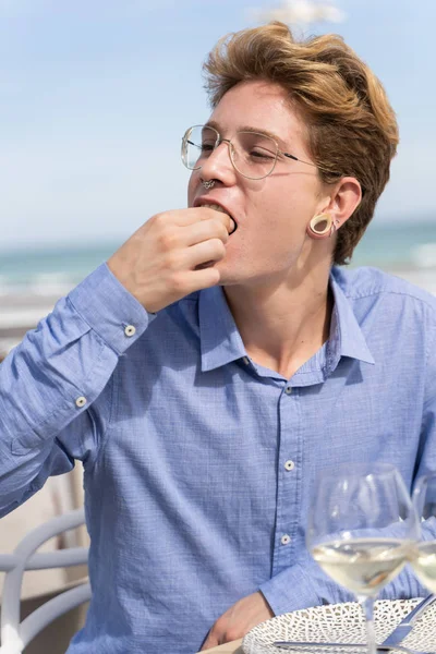 照片上的年轻人手拿着叉子和眼镜 手拿着寿司食品 在海边一家餐馆的阳台上 手里拿着酒杯 愉快地吃着寿司 — 图库照片
