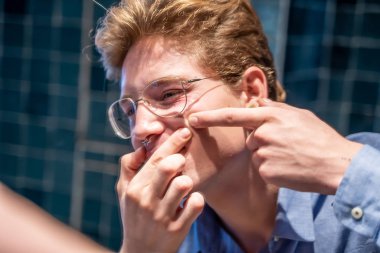 Genç bir adam banyoda aynanın önünde sivilce çıkarıyor.