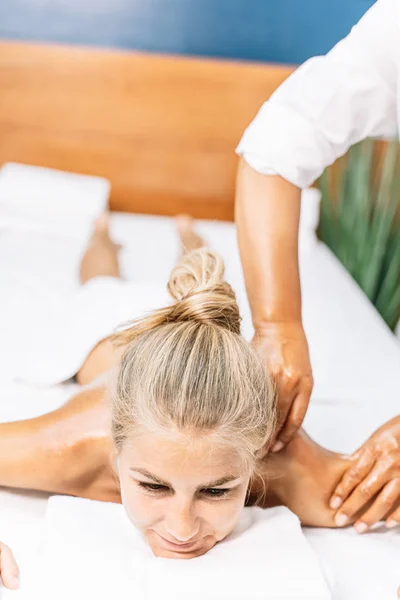 Vertical photo of a blonde girl lying down while she gets a back massage