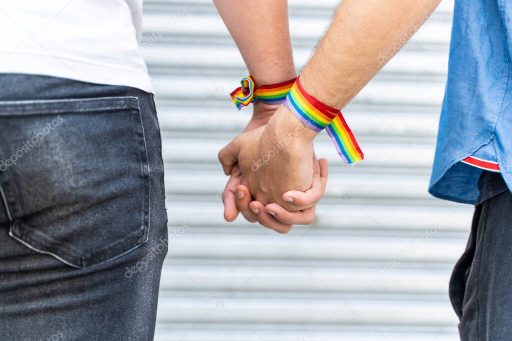 Detail of two men holding hands with lgtb rainbow flag bracelets.