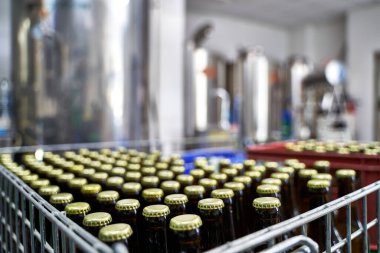 Bira fabrikasındaki çiğ bira şişelerine odaklan. Arka plandaki tüm makinelerin odaklanmadığı kutularda dağıtılmaya hazır olsun.