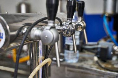 Bira fabrikasındaki makinelere bağlı siyah lastik saplı birkaç metalik musluğun seçici odak noktası