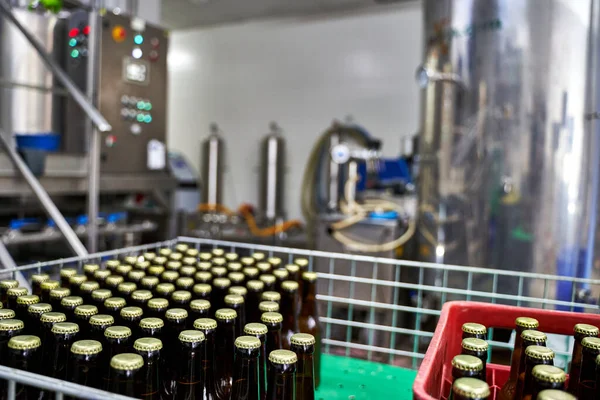 Selective focus on a group of capped beer bottles in a brewery ready to be distributed in boxes with all the machines unfocused on the background