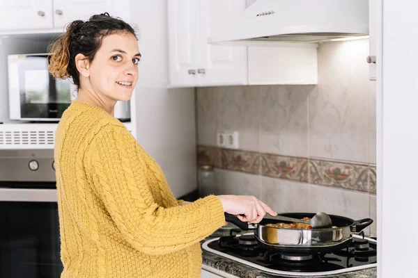 電子レンジの隣に立って微笑んで顔を右に回す黄色いセーター調理をしている妊婦 ストック写真