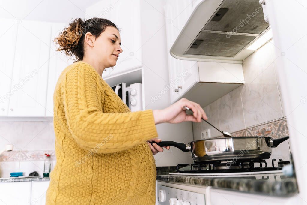 Counterpoint photo of pregnant woman with a yellow sweater cooking standing in a kitchen with serious expression