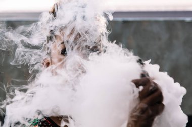 Beyaz ve derin duman kıvırcık saçlı siyah bir kızı gizliyor. Odada buharlı sigara içiyor.