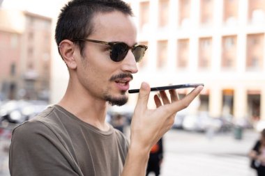 Güneş gözlüklü ve kulağını deldirmiş genç bir adam caddenin ortasında cep telefonu hoparlöründen konuşuyor.