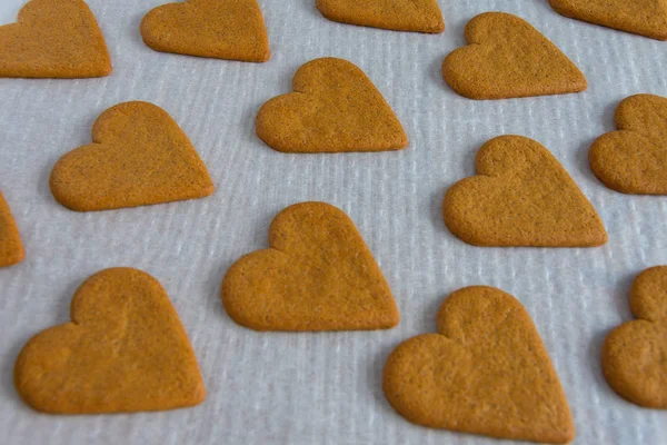 Top view of heart shaped gingerbread cookies on white baking paper in horizontal