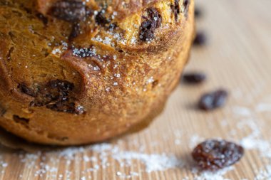 Ahşap zemin üzerinde çikolata parçacıkları ve yatay arkaplanda kuru üzüm ve şeker taneleri olan panettone 'a yakın çekim