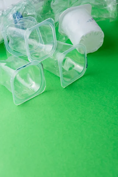 Top view of plastic containers on green background, ready for recycling, vertically with copy space