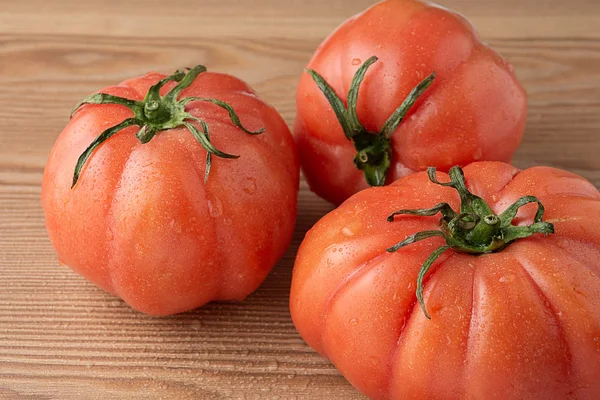 Üç pembe domatesin üst görüntüsü. Yatay olarak ahşap masanın üzerine su damlıyor.
