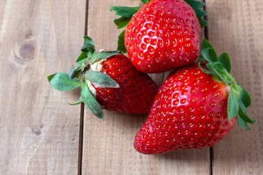 Üst manzara, ön planda, ahşap tahtada üç çilek, yatay olarak metin için yer var.