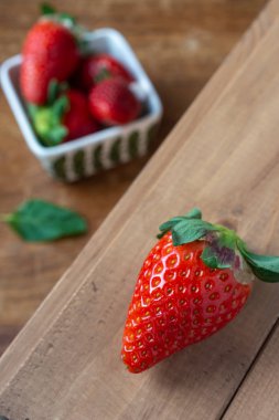 Odaklanmış çilek yakın plan, beyaz kasede çilek ve odak dışı nane yaprağı, ahşap tahta, dikey