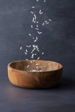 Beyaz pirincin yakın plan, gri arka plandaki ahşap kaseye düşüşü kopya alanı ile dikey.