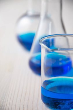 Mavi sıvı ve seçici odaklı üç cam test tüpü yakın plan, çözünmüş beyaz ahşap masa, dikey
