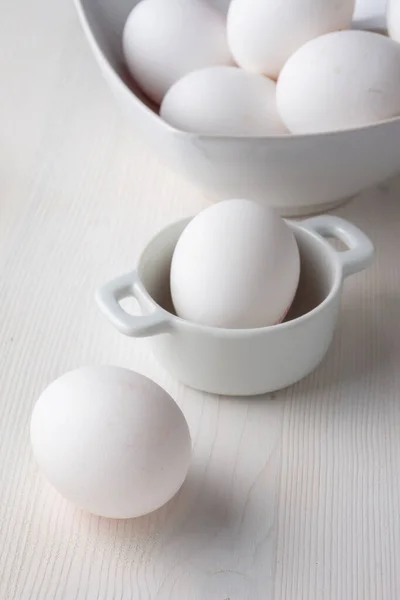 Top view of white eggs in a white bowls, with selective focus, on white wooden table in vertical