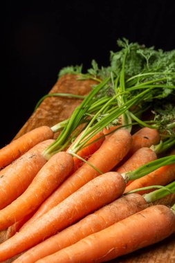 Yeşil yapraklı havuç manzarası, kırsal bir masa üzerinde, siyah arkaplan, dikey, kopyalama alanı ile
