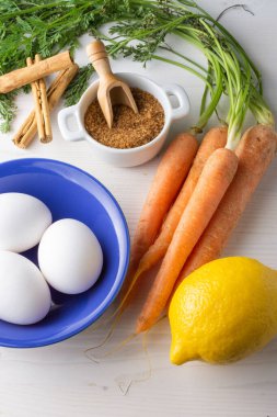 Malzemelerin havadan görünüşü, yumurta, havuç, un, limon, kahverengi şeker, tarçın, beyaz ahşap masa, dikey