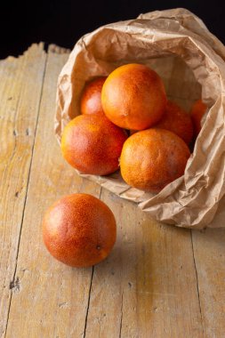 Kese kağıdındaki kan portakallarının üst görüntüsü, seçici bir odak ile, kırsal ahşap tahta ve siyah arka plan, dikey