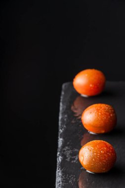 Üç ıslak ve çizgili kumato kiraz domatesinin hava görüntüsü, seçici bir odak ile, dikey siyah arkaplan ve siyah arkaplan üzerine, kopyalama alanı ile