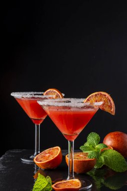 İki kan portakallı martini bardağının üst görüntüsü, yarı portakallı ve naneli, siyah arka planda, dikey, kopyalama alanı olan.