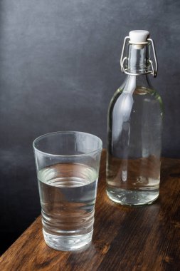 Cam ve cam şişenin üst görüntüsü koyu ahşap masa üzerinde su ve gri arka plan, dikey, kopyalama alanı ile