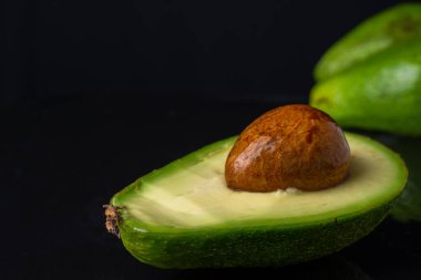 Tohumlu yarım yeşil avokado, ıslak siyah levhada, yatay.