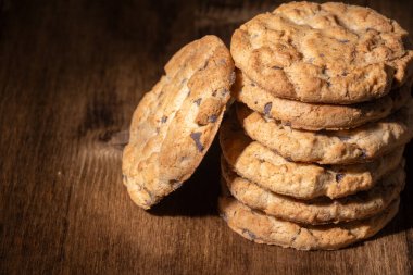 Çukulata parçalı kurabiyeleri üst üste, ahşap masada, karanlık ışıkta, yatay ve fotokopi uzayı ile yakın çekim yap.