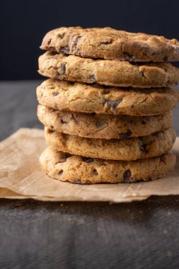 Çukulata parçalı kurabiyelerin kağıt ve koyu masa örtüsü üzerinde, dikey, kopyalama alanı ile yakın plan