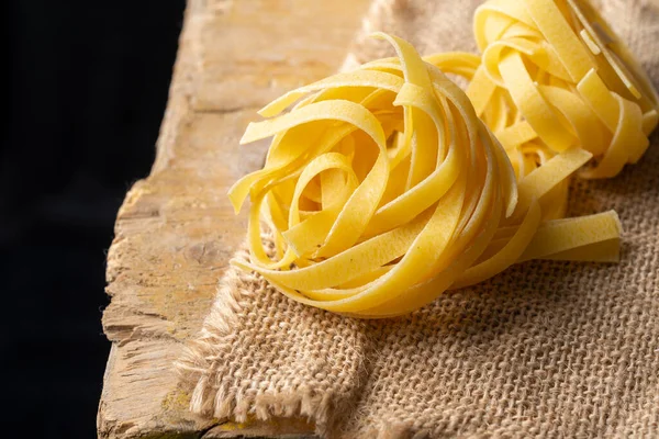 Top View Raw Tagliatelle Nests Burlap Rustic Table Black Background — Stock Photo, Image