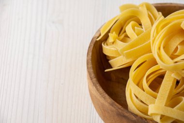 Ham tagliatelle ile ahşap kasenin üst görüntüsü, beyaz ahşap masa üzerinde, yatay, kopyalama alanı ile