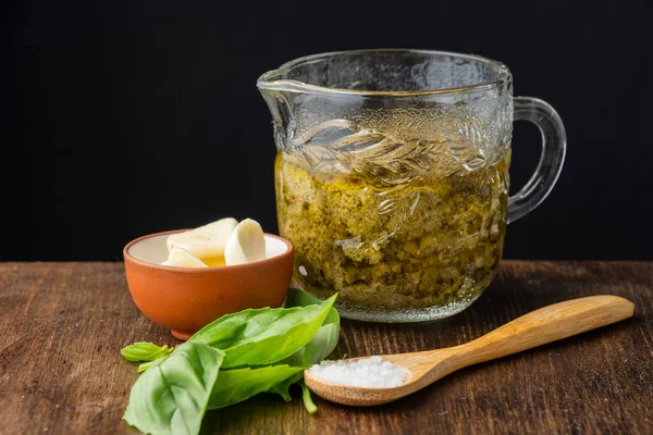 Pesto soslu cam kavanoz, sarımsak, fesleğen ve ahşap kaşık, ahşap masa, siyah arka plan, yatay kaşık.