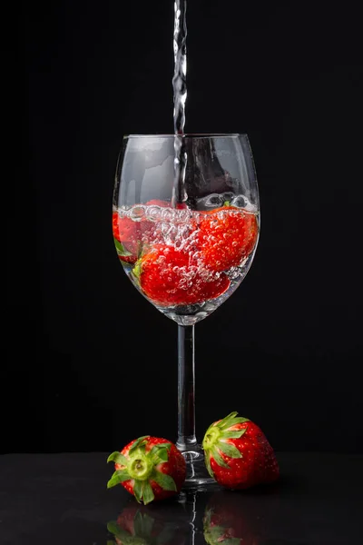 玻璃杯与草莓近照 水落石出 两个草莓 在石板上 黑色背景 — 图库照片