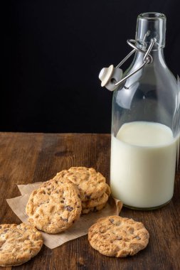 Kahverengi kağıt üzerinde çikolatalı kurabiyelerin üst görüntüsü ve koyu ahşap masa süt, siyah arka plan, dikey