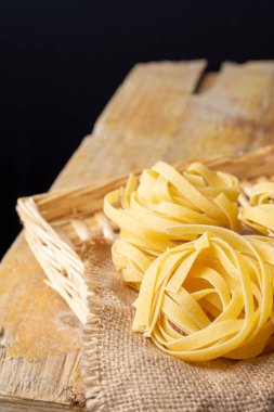Çiğ tagliatelle yuvalarının üst görüntüsü çuval, sepet ve kırsal ahşap masa, siyah arkaplan, dikey