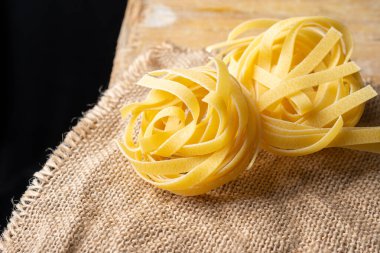 Çuval bezi ve kırsal ahşap masa üzerindeki çiğ tagliatelle yuvalarına yakın plan, siyah arkaplan, yatay