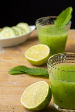 Salatalık suyu, misket limonu, nane ve salatalık dilimleri, seçici odaklı, ahşap masa, siyah arka plan, dikey