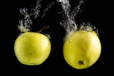 İki yeşil elma suya düşer ve siyah arka planda kabarcıklar olur.