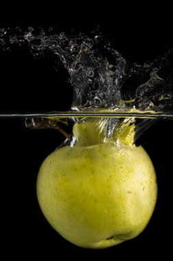 Bir yeşil elma suya düşer ve siyah arka planda kabarcıklar olur.