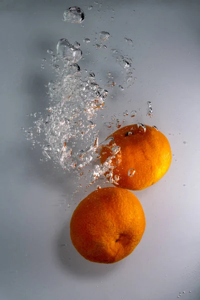 Zwei Mandarinen, die mit Blasen auf weißem Hintergrund ins Wasser fallen — Stockfoto