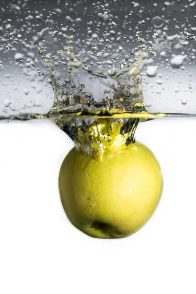 Одно зеленое яблоко падает в воду с брызгами и пузырьками на белом градиентном фоне — стоковое фото