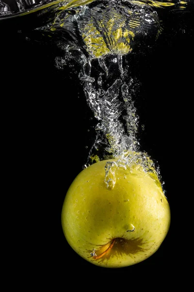 Одно зеленое яблоко падает в воду с пузырьками на черном фоне — стоковое фото