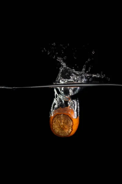 Один фундук падает в воду с брызгами и пузырьками на черном фоне — стоковое фото