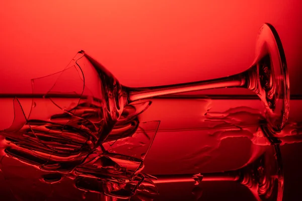 Kırık şarap kadehi kırmızı arka plandaki cam ayna masasında yatıyor. — Stok fotoğraf
